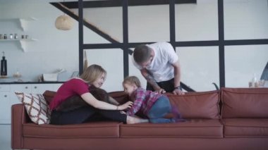 Gülümseyen beyaz adamın portresi. Karısına ve kızına kanepede oynayan adama hayran. Mutlu sarışın kadın ve küçük tatlı kız koltukta oturmuş baba gibi konuşuyorlar. Aile eğlencesi..