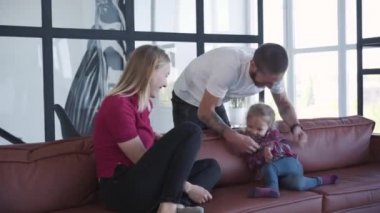 Neşeli gülen adam ve kadın evdeki kanepede oturan sevimli kızı gıdıklıyor. Hafta sonları birlikte eğlenen neşeli beyaz bir ailenin portresi. Bağlanma, birlik, yaşam tarzı, neşe.