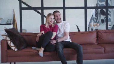 At kuyruklu küçük kız kanepede oturan erkek ve kadına sarılıyor. Kafkasyalı genç bir aile hafta sonları evde boş vakit geçiriyor. Eğlence, eğlence, yaşam tarzı, eğlence, mutluluk..