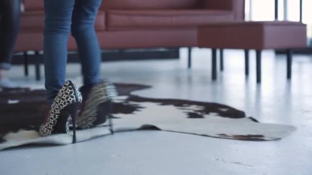 Vista trasera de la pequeña chica caucásica caminando en tacones altos hasta el sofá. Joven hombre y mujer sonrientes sentados en el sofá y admirando a su hija disfrutando los fines de semana en casa. Estilo de vida, ocio, infancia . — Vídeo de stock