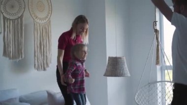 Sarışın, gülümseyen bir kadın ve yatağa atlayan küçük bir kızın portresi. Neşeli beyaz anne-kız yatak odasında baba ve kocayla eğleniyor. Boş zaman, dinlenme, yaşam tarzı, aile.