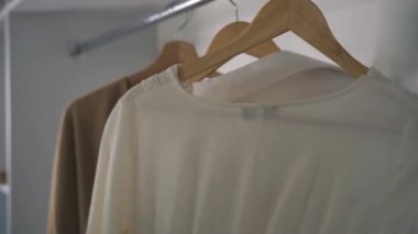 Beyaz kadın eli, gardıroptaki askılarda elbise seçiyor. Tanınmayan genç bir kadın sabah evde hazırlanıyor. Moda, yaşam tarzı, tarz.