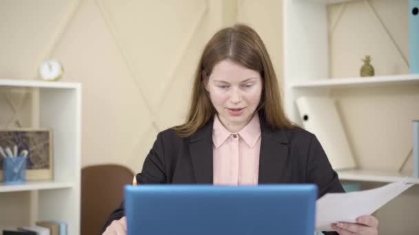 Sonriendo joven mujer caucásica de acuerdo con alguien en el chat inalámbrico y hablando. Retrato del empleado pelirrojo comunicándose en línea mientras la cámara se aleja mostrando la habitación desordenada. Trabajo remoto, freelance . — Vídeo de stock