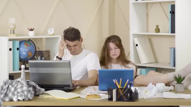 Jonge uitgeputte man en vrouw die surfen op internet. Portret van een blanke brunette en een roodharige meid in vieze kleren met laptops binnenshuis. Weekend vrijetijdsbesteding, werken op afstand, freelance. — Stockvideo