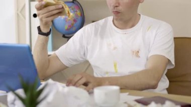 Pizza yiyen ve dizüstü bilgisayarda yazan tanınmamış bir adam. İnternette sörf yapan beyaz, genç bir erkek. Sosyal medya kullanan, kirli tişörtlü rahat bir adam. Yaşam tarzı, cihaz bağımlılığı.
