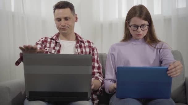 Plano medio de joven pareja caucásica cerrando laptops y abrazando. Feliz hombre y mujer milenarios sonrientes descansando juntos. Amor, ocio, estilo de vida . — Vídeos de Stock