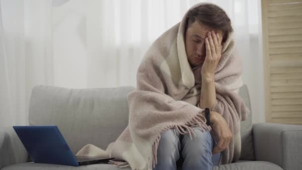 Portrait d'un homme caucasien malade enveloppé dans une couverture éternuant et frottant les yeux. Brune malade souffrant de grippe, pandémie de Covid-19. Médecine, santé, fièvre, épidémie de coronavirus. — Video