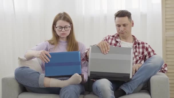 Jonge verslaafde man en vrouw die laptops openen en typen op toetsenborden. Portret van mannelijke en vrouwelijke millennials surfen op internet of met behulp van sociale media. Apparaatverslaving, levensstijl. — Stockvideo