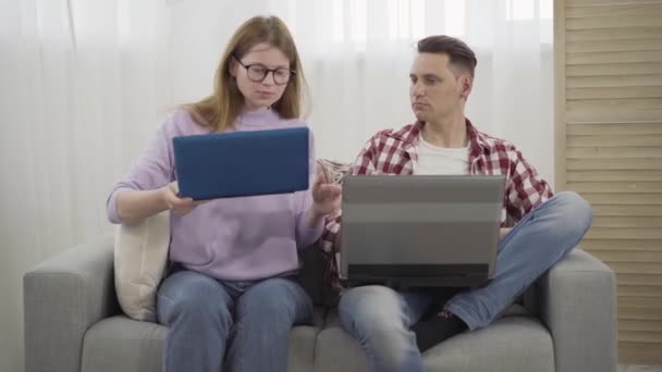 Jonge roodharige millennial vrouw in bril vraagt vriendje om hulp met laptop. Zelfverzekerde brunette Kaukasische man typt op toetsenbord en praat met vriendin. Portret van gelukkig stel thuis. — Stockvideo