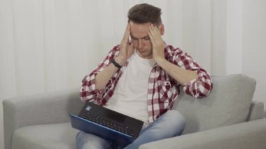 Tükenmiş Kafkas esmer adam şakakları ovuyor ve dizüstü bilgisayar ekranına bakıyor. İnternette sörf yapan yorgun beyaz adamın portresi. Uzaktan çalışma, serbest çalışma, yaşam tarzı, aşırı çalışma.