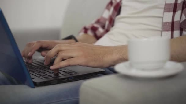 Primer plano de las manos masculinas escribiendo en el teclado del ordenador portátil. Hombre caucásico joven irreconocible tomando taza de café como trabajo en línea en casa. trabajo remoto, freelance, confianza, éxito . — Vídeos de Stock