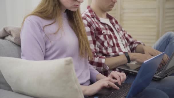 Nierozpoznawalny młody mężczyzna i kobieta piszący na klawiaturze laptopa w nowoczesnym biurze lub w domu. Wolni strzelcy lub pracownicy siedzący na kanapie i pracujący online. Styl życia, praca, praca zdalna. — Wideo stockowe