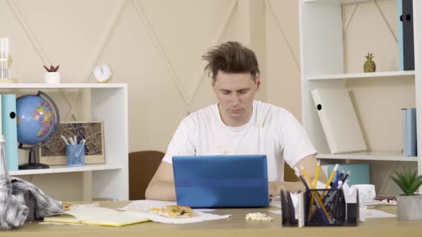 若い疲れた男がキーボードのキーを押し、ノートパソコンを閉じて椅子にもたれています。疲れが、リモートオンライン作業を終えた汚れた服で満足フリーランサーの肖像画。フリーランス、ライフスタイル. — ストック動画
