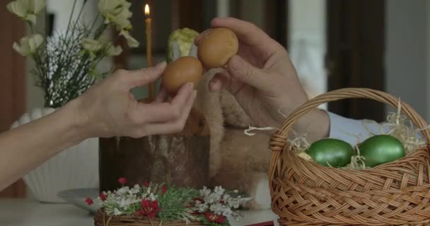 Male and female hands knocking eggs on Easter. Close-up side view of unrecognizable Caucasian man and woman performing tradition indoors. Traditional celebration, holy holiday, lifestyle. — Stock Video