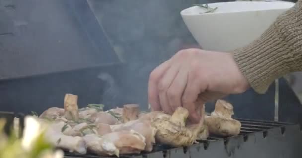 Onherkenbare man zet rauw vlees en champignons op barbecue rooster. Mannelijke hand leggen kip en groenten op bbq grill buiten. Lekker eten, koken, barbecueën. — Stockvideo