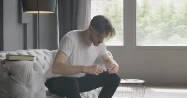 Genç sakallı adam odaya giriyor, gözlük takıyor ve kitap açıyor. Evde edebiyat okuyan esmer, kendinden emin bir erkek okuyucunun portresi. Zeka, eğitim, yaşam tarzı. Sinema 4k ProRes Merkezi.