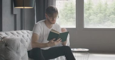 Saçını evde kitap okumak gibi ayarlayan yakışıklı bir adam. Esmer beyaz tenli genç okuyucunun portresi evde edebiyatla dinleniyor. Yaşam tarzı, hobi, zeka. Ağır çekim. Sinema 4k Karargahı.