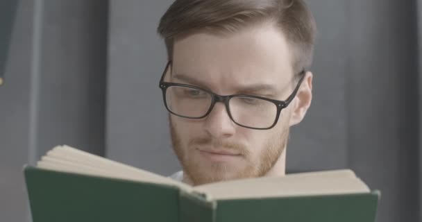 Cara de primer plano del joven inteligente en anteojos leyendo libro. Retrato de morena barbuda lectora caucásica disfrutando de la literatura en interiores. Estilo de vida, afición, inteligencia, educación. Sede del cine 4k ProRes . — Vídeos de Stock