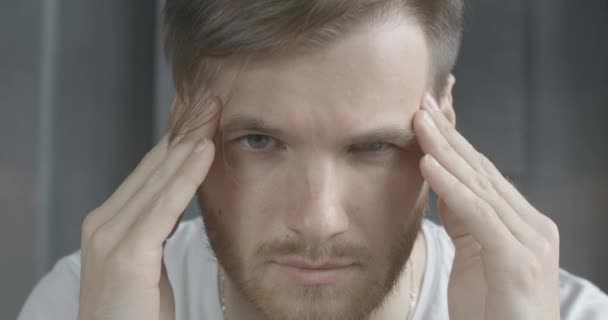 Extremo primer plano de morena hombre caucásico con los ojos grises frotando las sienes. Retrato de un joven guapo barbudo con dolor de cabeza severo. Atención médica, exceso de trabajo, estrés, tensión. Sede del cine 4k ProRes — Vídeos de Stock