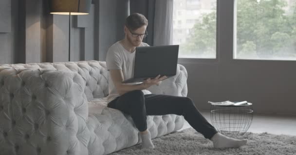 En cámara lenta, un joven usando un portátil y mirando a través de documentos en el interior. Retrato lento de guapo profesional freelancer confiado navegando por Internet. Trabajo remoto, estilo de vida. Sede del cine 4k ProRes . — Vídeos de Stock