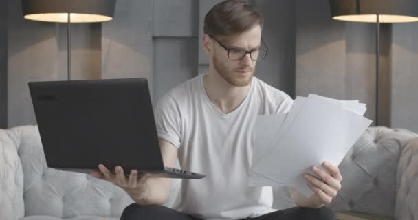 Zenuwachtige jonge blanke man die documenten in slow motion opgeeft als kijkend naar het laptopscherm. Portret van gestresste knappe zakenman freelancer die thuis online werkt. Cinema 4k ProRes Hoofdkwartier. — Stockvideo