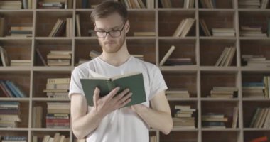 Gözlüklü, kendine güvenen beyaz bir adamın kitap sayfasını çevirip gülümsediği bir fotoğraf. Kütüphanede edebiyat okuyan odaklanmış bir gencin portresi. Hobi, zeka. Sinema 4k ProRes Merkezi.