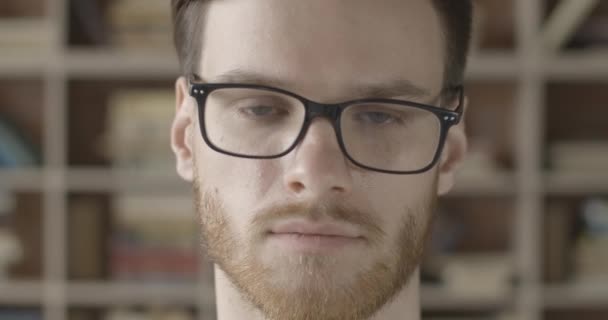 Cara de cerca extrema del guapo moreno quitándose las gafas en cámara lenta. Retrato de tipo caucásico inteligente con barba roja mirando a la cámara en la biblioteca. Sede del cine 4k ProRes . — Vídeo de stock