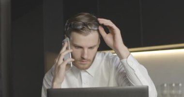 Yavaş yavaş kendine güvenen bir adam telefonda konuşuyor ve bilgisayar ekranına bakıyor. Kafkasyalı ciddi bir iş adamının portresi akıllı telefondan projeyi tartışıyor. Sinema 4k ProRes Merkezi.