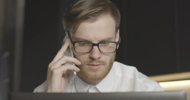 Ανήσυχος άνθρωπος με αυτοπεποίθηση με γυαλιά που μιλάει στο τηλέφωνο και κοιτάζει την οθόνη του φορητού υπολογιστή. Κοντινό πλάνο πορτρέτο του συγκεντρωμένου Καυκάσου επιχειρηματία που έχει επαγγελματικά προβλήματα. Κινηματογράφος 4k ProRes HQ. — Αρχείο Βίντεο