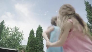 Güzel ikiz kardeşler el ele tutuşuyor, yaz gökyüzünün arka planında zıplıyor ve dönüyorlar. Güneşli bir günde dışarıda eğlenen neşeli çocukların alt manzarası. Eğlence, eğlence, güzellik.