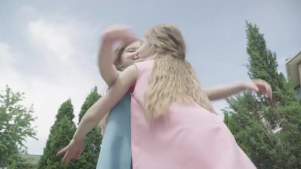 Vista inferior de los encantadores gemelos pequeños abrazándose al fondo del cielo azul de verano. Sonrientes chicas caucásicas abrazándose al aire libre. Tiempo libre en familia, felicidad, estilo de vida, alegría . — Vídeos de Stock