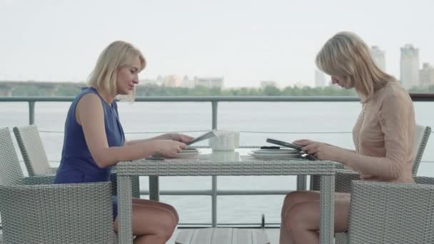 Vue latérale vue générale de femmes d'affaires confiantes discutant menu dans un restaurant en plein air. Portrait de femmes caucasiennes prospères reposant dans un café luxueux sur la rive de la rivière. Luxe loisirs, mode de vie. — Video