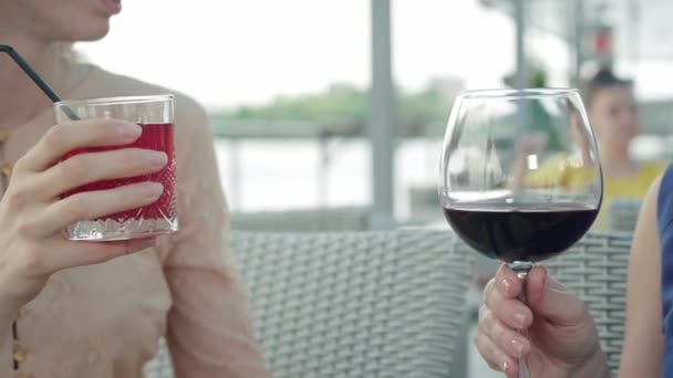 Close-up van vrouwelijke handen klinkende glazen met dranken in outdoor cafe. Onherkenbare blanke vrouwen vieren vakantie in restaurant aan de oever van de rivier buiten. Vrije tijd, geluk, vreugde. — Stockvideo