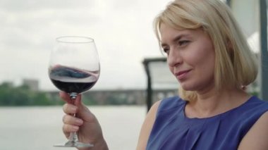 Açık havada kırmızı şaraptan hoşlanan gülümseyen sarışın kadının yakın çekimi. Açık deniz restoranında içki içen zarif beyaz bir bayanın yan görüntüsü. Boş zaman, dinlenme, yaşam tarzı, neşe.