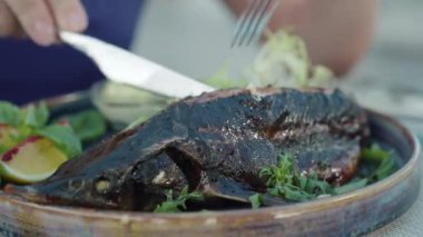 Restoranda tabakta pişmiş balık var. Çatal ve bıçaklı kadın elleri çanaktan bir parça alıyor. Kafede nefis yemekler. Gıda endüstrisi, iş dünyası, aşçılık, mutfak.