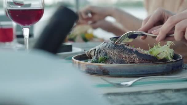 Vista lateral de cerca de las manos femeninas cortando pescado frito en el plato. Mujer irreconocible comiendo sabroso esturión al horno delicioso en el restaurante al aire libre. Omega-3, dieta, delicatessen . — Vídeos de Stock