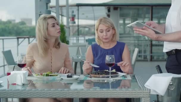 Retrato de mujeres elegantes pidiendo postre en la cafetería al aire libre. Camarero masculino irreconocible tomando la orden de los clientes ricos utilizando tableta. Negocio moderno de restaurantes, estilo de vida, riqueza, lujo . — Vídeo de stock