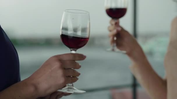 Nerozpoznatelné ženy cinkají sklenicemi s vínem a popíjejí nápoje v bouřlivý den ve venkovní restauraci. Dva kavkazští přátelé slaví něco v kavárně s nápojem. Životní styl, volný čas, radost. — Stock video