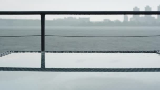 雨の曇りの日にグレーの桟橋。嵐の下を流れる川の水。背景には都市がぼやけている。自然、天気、気候、うつ病の概念. — ストック動画