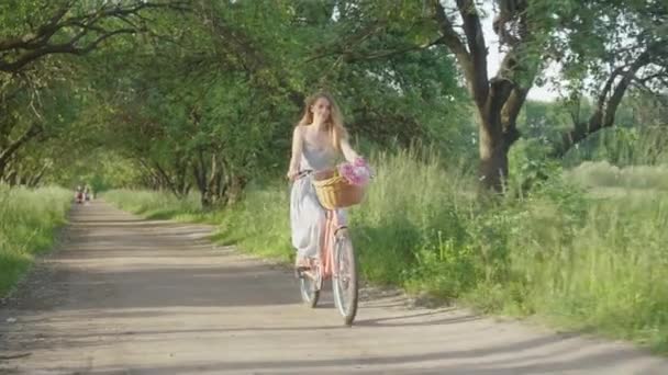 Amplio tiro de encantadora joven mujer caucásica montar en bicicleta en el parque de verano. Retrato de dama delgada positiva sonriente en vestido disfrutando de un día soleado al aire libre. Alegría, ocio, estilo de vida, belleza . — Vídeos de Stock