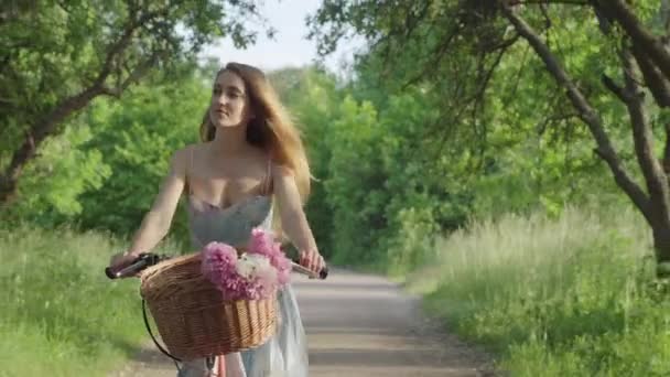 Confident young brunette woman riding bicycle along the alley in sunny summer park. Portrait of elegant charming Caucasian girl enjoying velo trip outdoors. — Stock Video