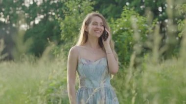 Güneşli çayırda telefonla konuşan güzel bir kız. Beyaz tenli genç bir kadının portresi. Hafta sonu açık havada dinleniyor. Boş zaman, rahatlama, sükunet..