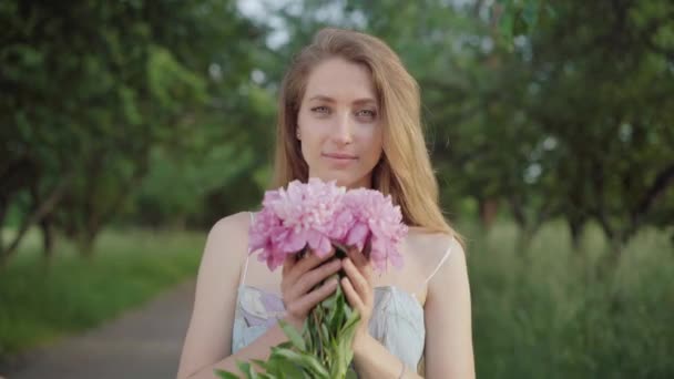 Bella giovane donna profumata bouquet di fiori nel parco estivo. Ritratto di affascinante signora bruna caucasica godendo la giornata di fine settimana all'aperto. Bellezza, tempo libero, stile di vita, gioia. — Video Stock