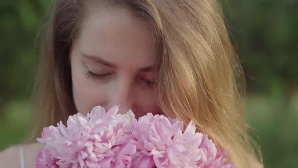 Faccia di primo piano estrema di bella donna che odora di fiori. Ritratto di affascinante ragazza caucasica in posa con bouquet all'aperto nella soleggiata giornata estiva. Felicità, svago, bellezza, stile di vita. — Video Stock