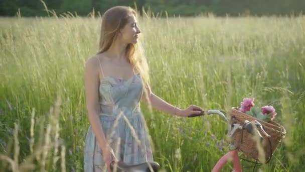 Vue latérale de jolie femme profitant de la lumière du soleil sur la prairie d'été. Portrait de belle jeune fille caucasienne debout dans un parc ensoleillé avec vélo et regardant loin avec les yeux fermés. — Video