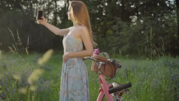 Ritratto laterale di giovane donna che fotografa la natura nel parco estivo al tramonto. Bruna sorridente ragazza caucasica in abito retrò fotografare prato al tramonto. — Video Stock