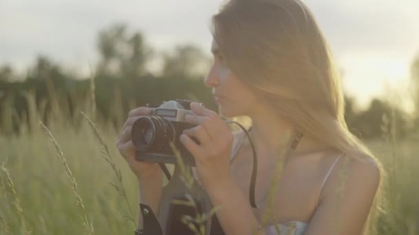 Detailní záběr brunetky fotografující na slunci v letním parku. Portrét mladé bělošky, jak fotí při západu slunce na louce. Hobby, životní styl, fotograf. — Stock video