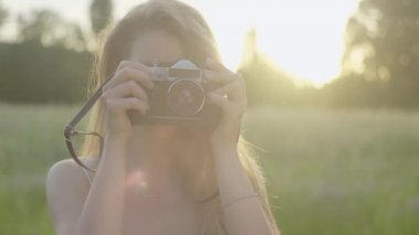 Kameralı bir kadının güneş ışınlarıyla fotoğraf çekerken ön görüntüsü. Güneş batarken manzaranın tadını çıkaran genç, pozitif beyaz kadın fotoğrafçının yakın çekimi..