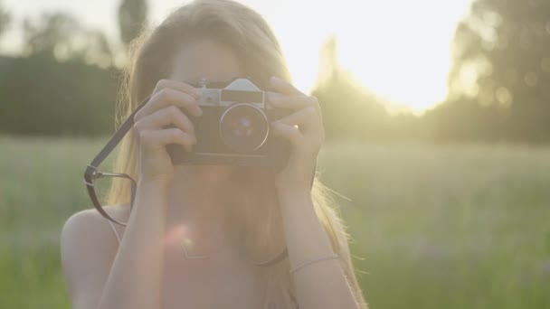 Vista frontal retrato de mulher com câmera tirando foto em raios de sol. Close-up de jovem fotógrafa caucasiana positiva desfrutando de fotografia de paisagem ao pôr do sol . — Vídeo de Stock