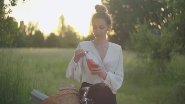 Középső lövés elegáns nő formalwear figyelembe palack gyümölcslé és ivás napnyugtakor. A gyönyörű fehér üzletasszony portréja a parkban pihen. Életmód, önbizalom, szabadidő. — Stock videók